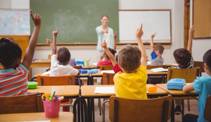 In classe, alunni con BES alzano la mano mentre l'insegnante guida una lezione di italiano e storia con partecipazione e attenzione collettiva.