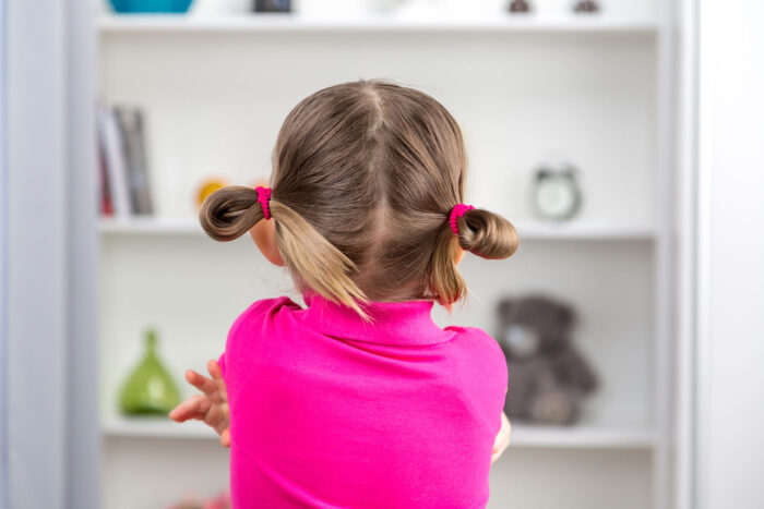 Una bambina con doppie codine e maglia fucsia è ripresa di spalle davanti a una mensola bianca, in un contesto legato all'ADHD nei bambini.